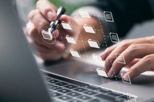 A person is using a pen to click on a folder icon on a virtual screen projected in front of their laptop.