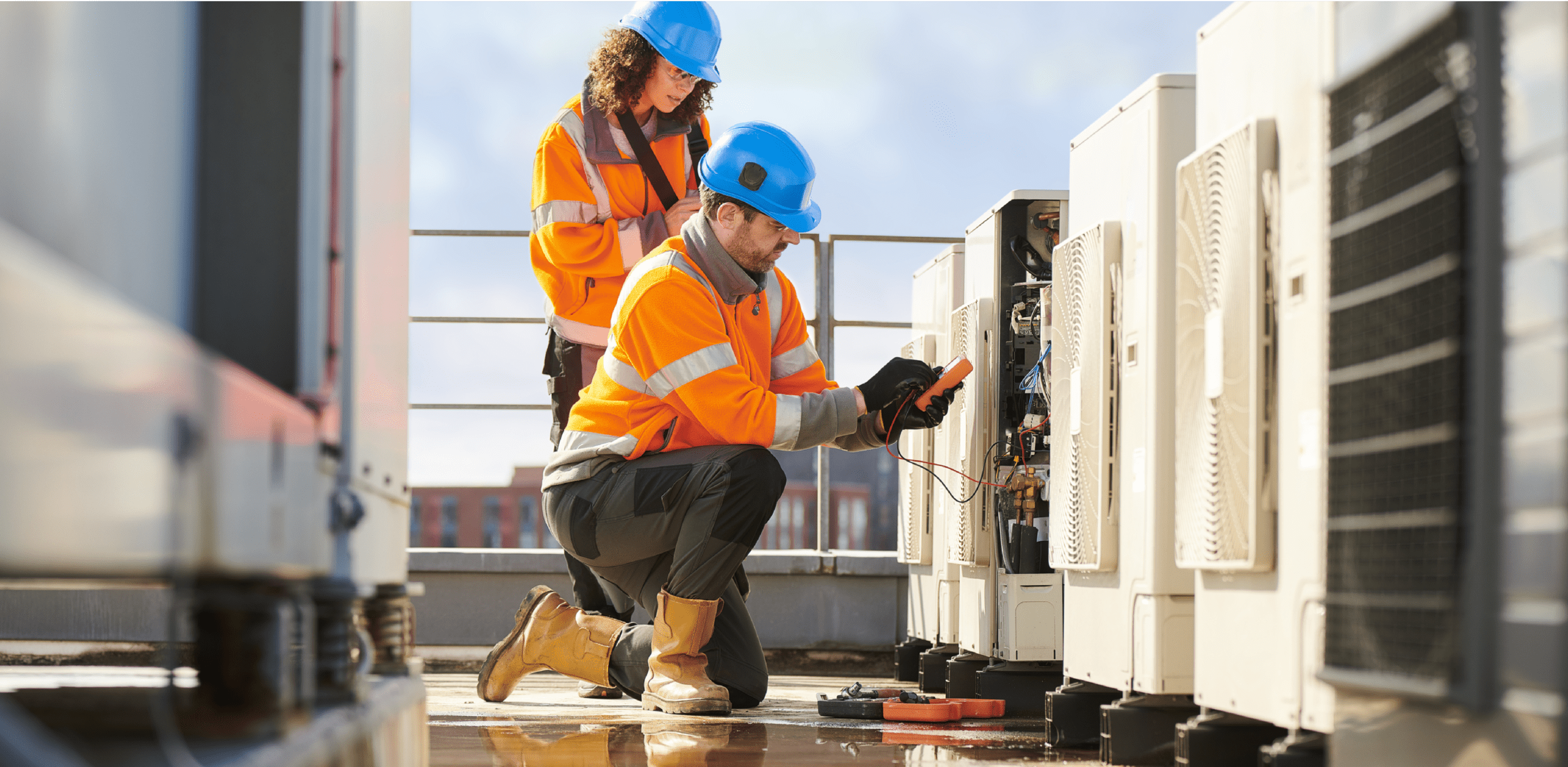 A woman and a man wearing safety helmets and jackets are on a rooftop working on something.